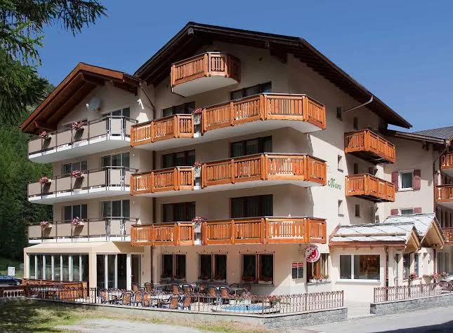 Exterior of Hotel Monte-Moro in Saas-Almagell with cream facade, wooden balconies and an outdoor terrace under a clear blue sky